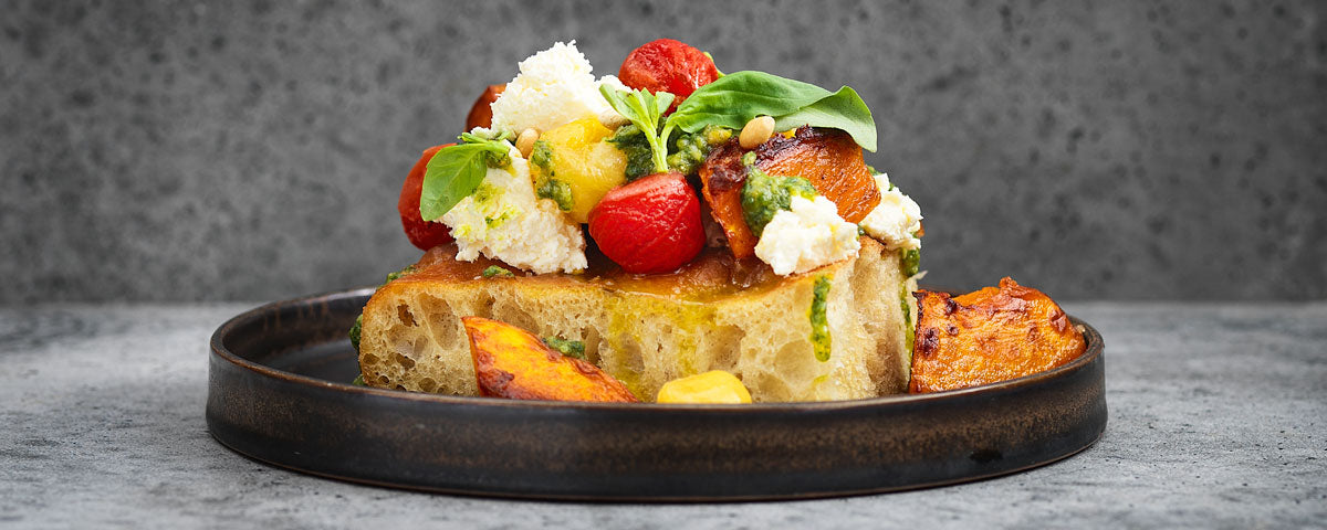 Billede af et stykke forcaccia, med topping af Loke, Havguspesto, græskarstykker og tomater. 