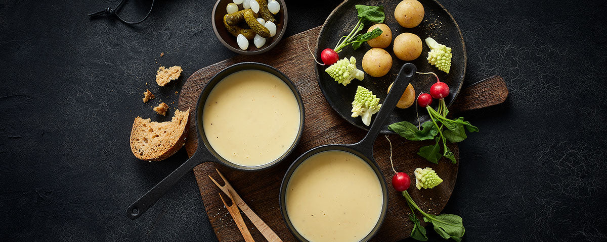 Billede af to små gryder med ostefondue og dertilhørende garniture til dyppelse. 