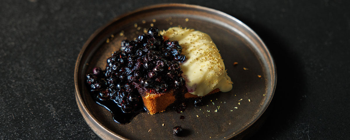 Billede af en skive sandkage, serveret med Den Hvide Dame og blåbær. 