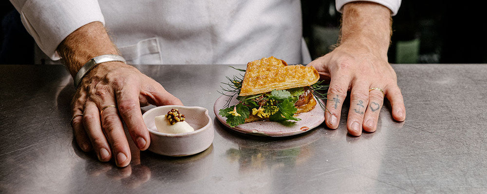 Billede af en kok der præsenterer en hjertevaffel-sandwich, med dertilhørende syltede sennepsfrø.