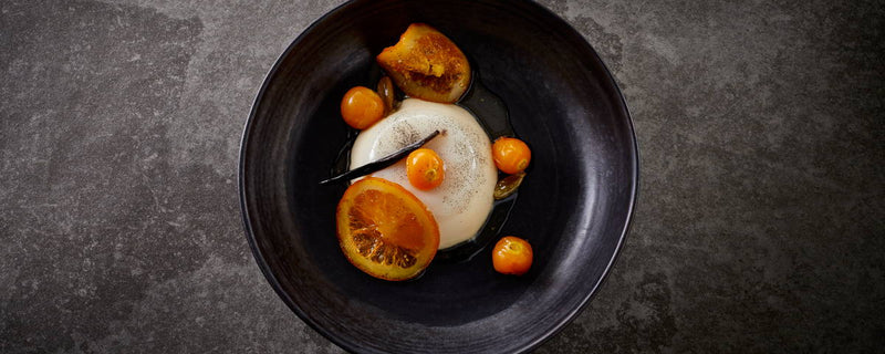 Billede af skål med Panna Cotta, serveret med skiver af appelsin. 