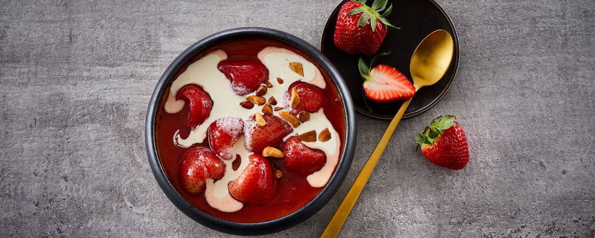 Billede af en rød og hvid jordbærgrød med fløde, serveret i skål med hele jordbær. 