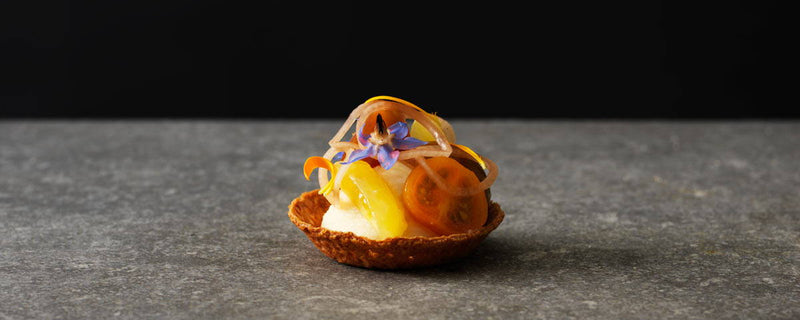 Billede af en lille sprød tartelet, med fyld af Gammel Knas Creme og toppet med tomat. 