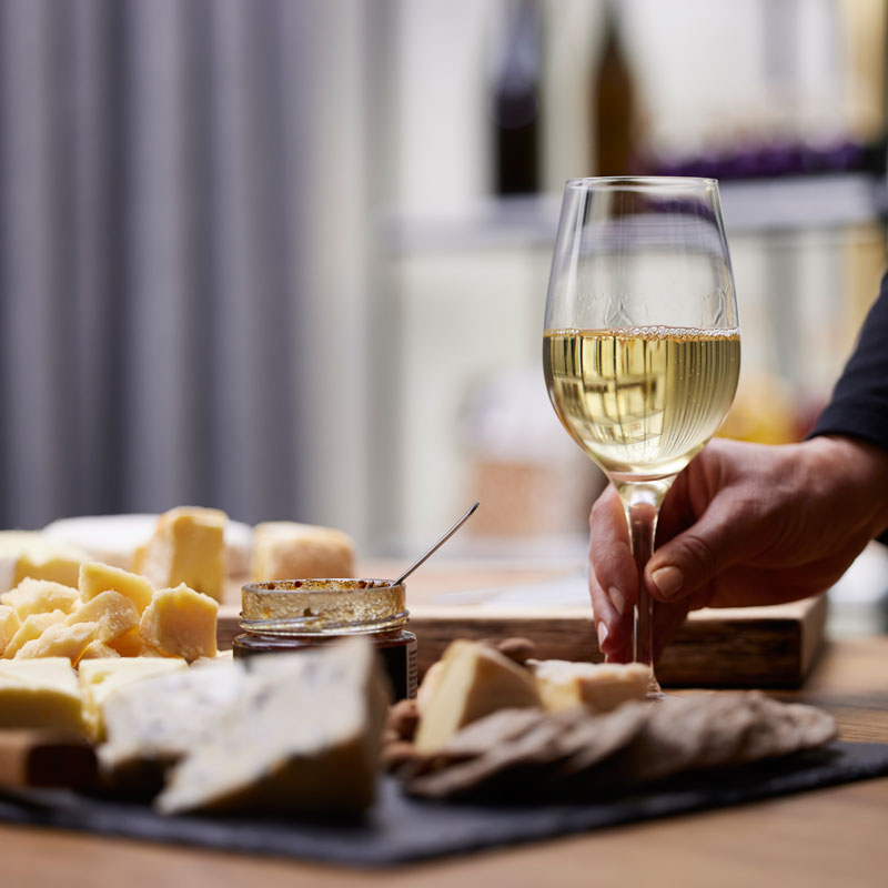 Ostebord med ostestykker og glas med hvidvin, hånd der rækker til