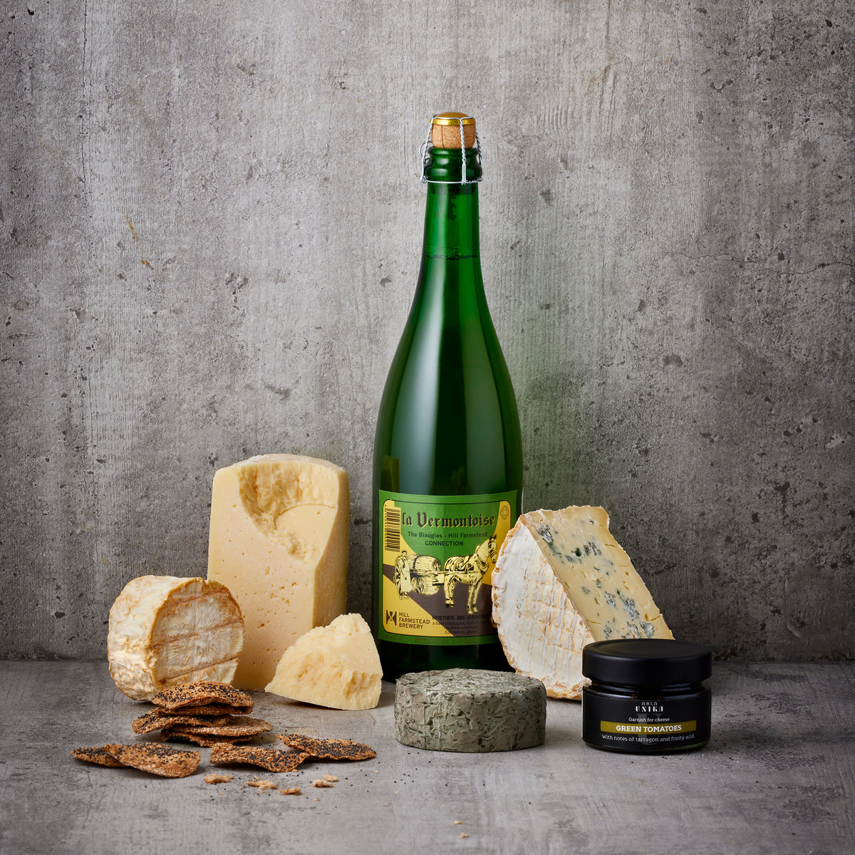 Ostebord med flere oste, sprøde kiks, grøn vinflaske og sort glas
